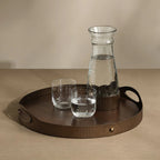 Glass carafe and two glasses on a wooden tray with a beige background